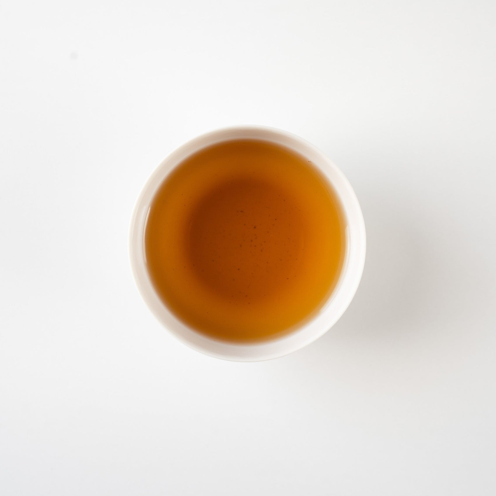 Top-down view of clear hojicha in a white teacup, revealing a gentle gradient of roasted amber tones.