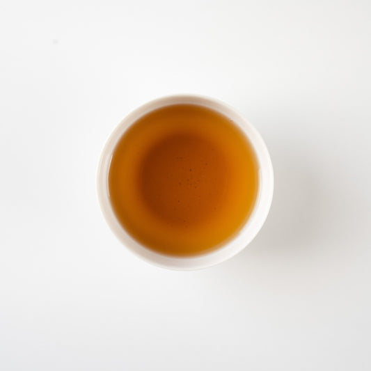 Top-down view of clear hojicha in a white teacup, revealing a gentle gradient of roasted amber tones.