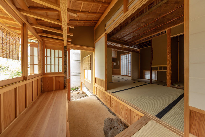 An expansive, light-filled tea space defined by exposed timber framing, sliding shoji screens, and layered architectural depth that embodies quiet restraint.