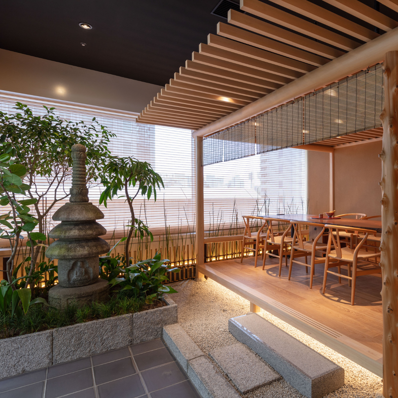 An elevated wooden salon framed by delicate reed screens and natural timber, looking out over a tranquil stone garden within a refined contemporary interior.