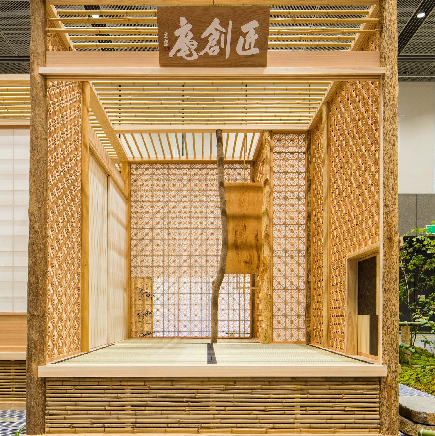 Pavillon de bois : murs de kumiko finement assemblés, poteaux à l’écorce conservée, sol de tatami et plaque sculptée à la main.