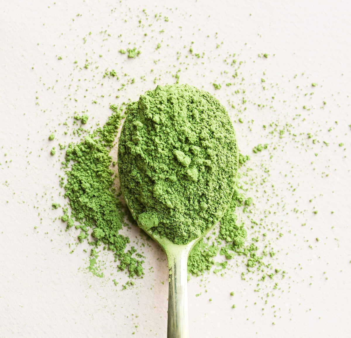 匙にすくった鮮やかな緑の抹茶。まわりに細かな粉が散る。