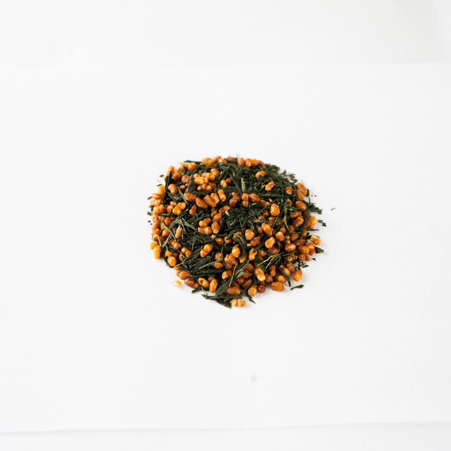 A neat pile of premium pesticide-free Genmaicha roasted rice green tea on a clean white surface, offering a fragrant, warming alternative to traditional Hojicha.