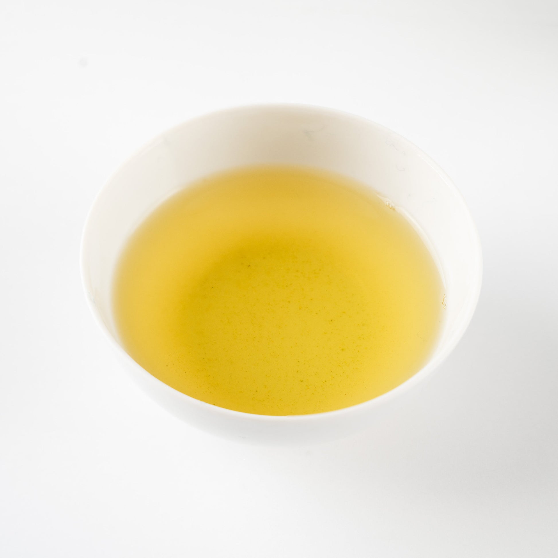 Clear golden-green liquor of brewed Sencha 'Nonokaze' in a simple white porcelain bowl, capturing its quiet clarity.