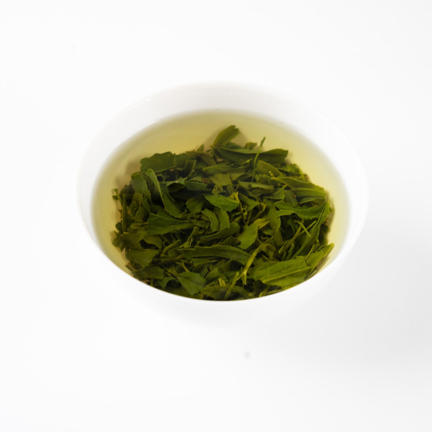 Angled view of steeped Sencha 'Nonokaze' green tea leaves blossoming gracefully in hot water within a white porcelain bowl.