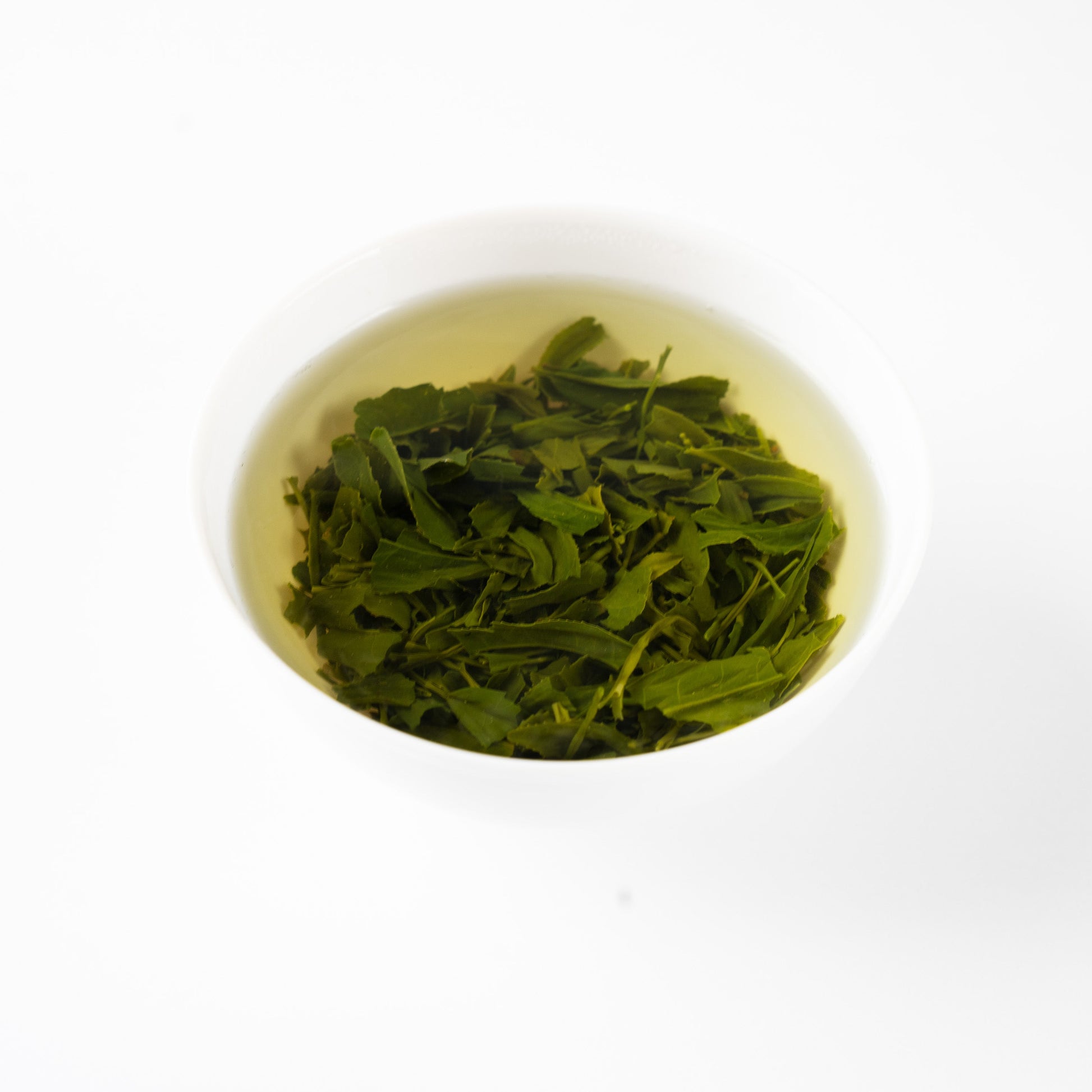 Angled view of steeped Sencha 'Nonokaze' green tea leaves blossoming gracefully in hot water within a white porcelain bowl.