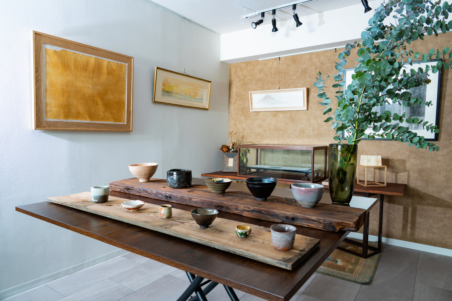 The intimate interior of wanova TOKYO, featuring curated contemporary ceramics set on weathered timber alongside artworks and understated greenery.