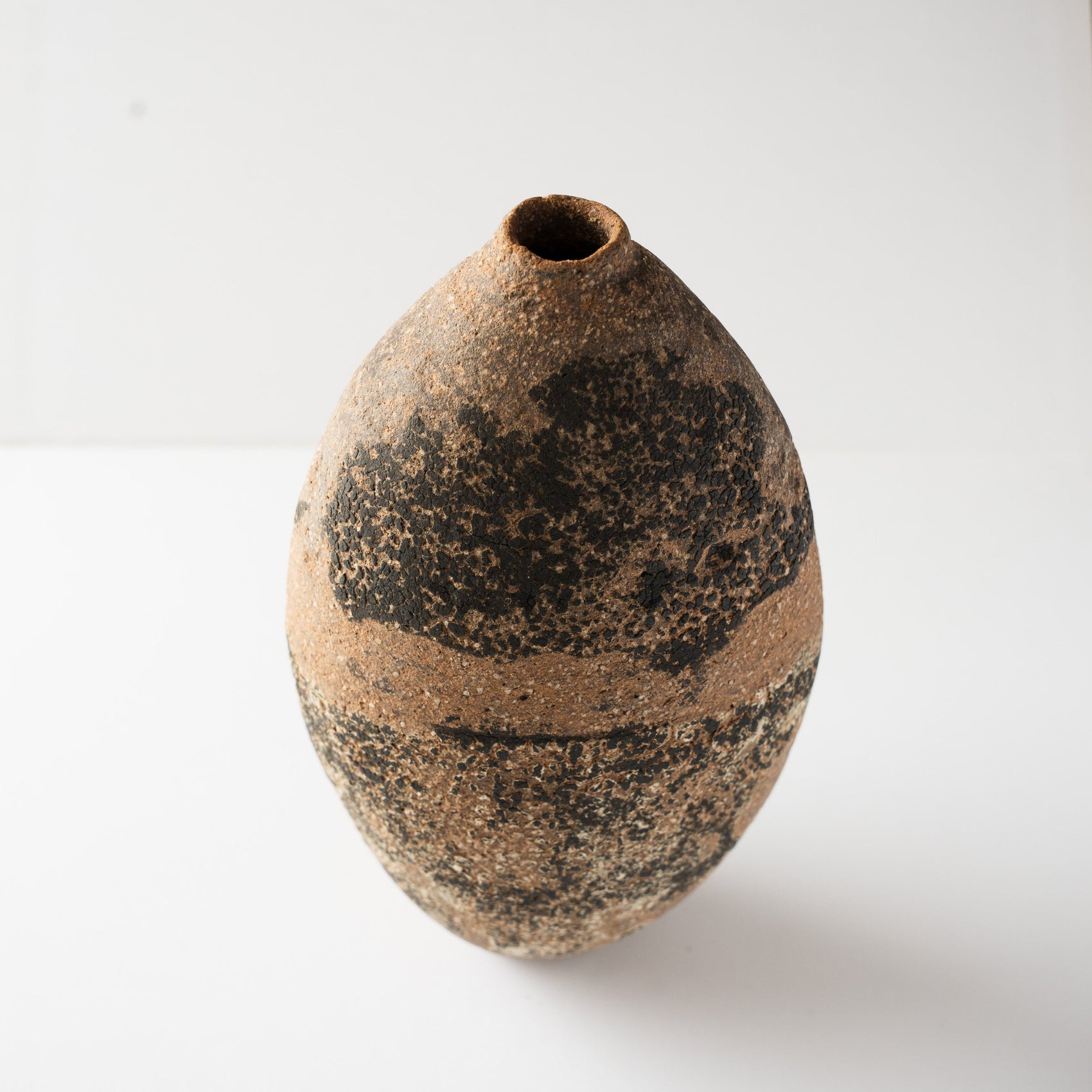 High-angle view of Wataru Myosyu's Genkoku HANAIRE vase, showing the organic seed-like form and dark tactile black glaze texture across the terracotta surface.