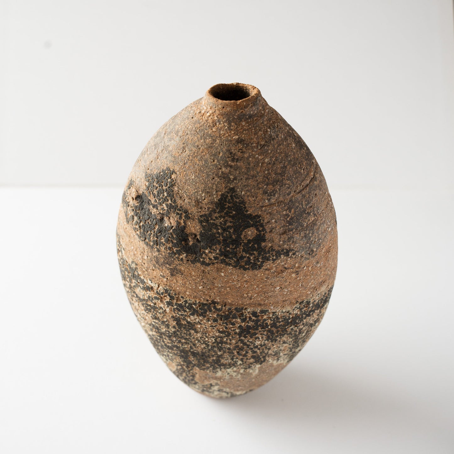 Turned high-angle perspective of the Genkoku ceramic vase by Wataru Myosyu, illustrating the contrasting coarse black band and reddish clay body.
