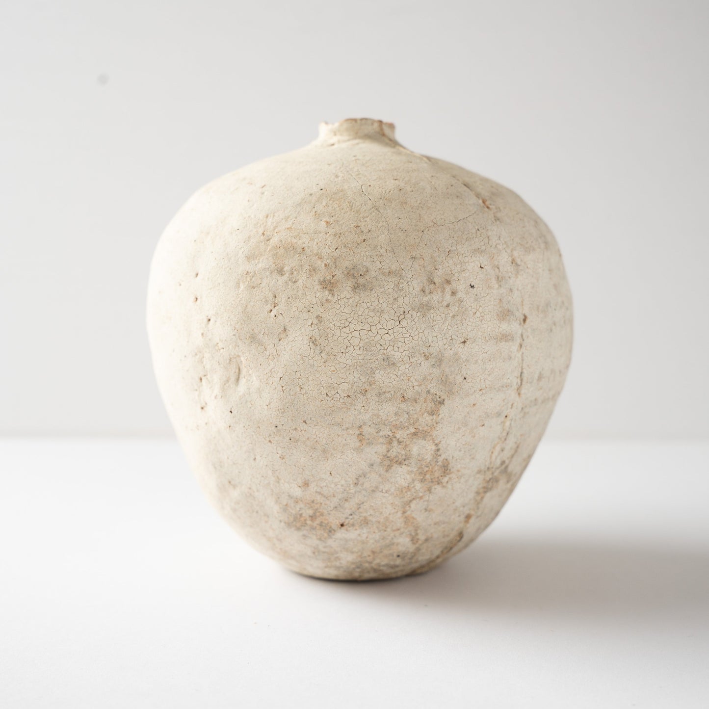 Eye-level side profile of Wataru Myosyu's Hakkoku Tada ceramic flower vase, highlighting the fruit-like spherical silhouette and chalky texture.