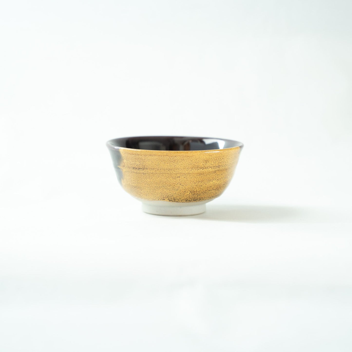 Profile view focusing on the golden-glazed surface of the GUINOMI, highlighting its fine, shimmering crystalline texture.