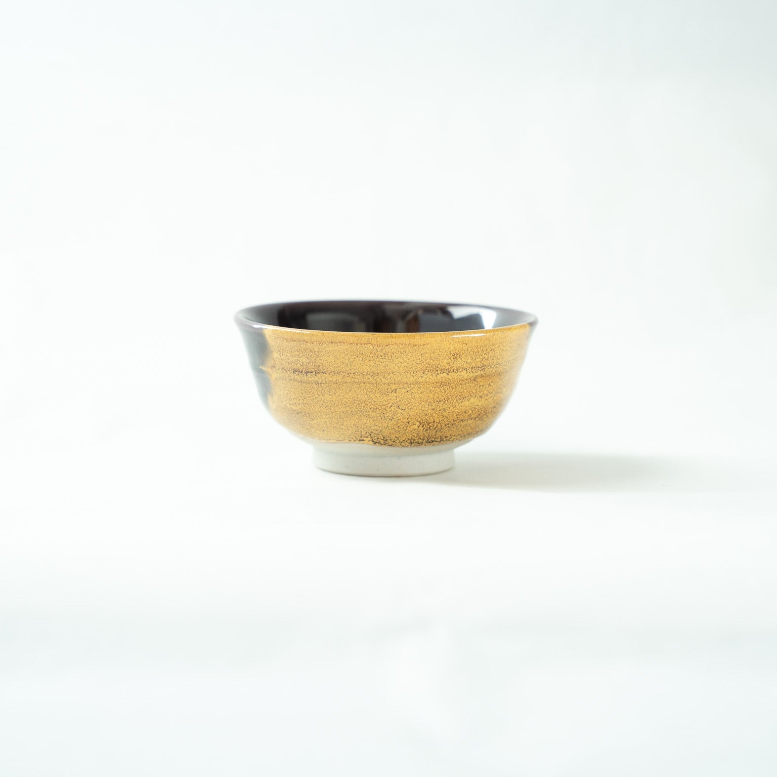 Profile view focusing on the golden-glazed surface of the GUINOMI, highlighting its fine, shimmering crystalline texture.