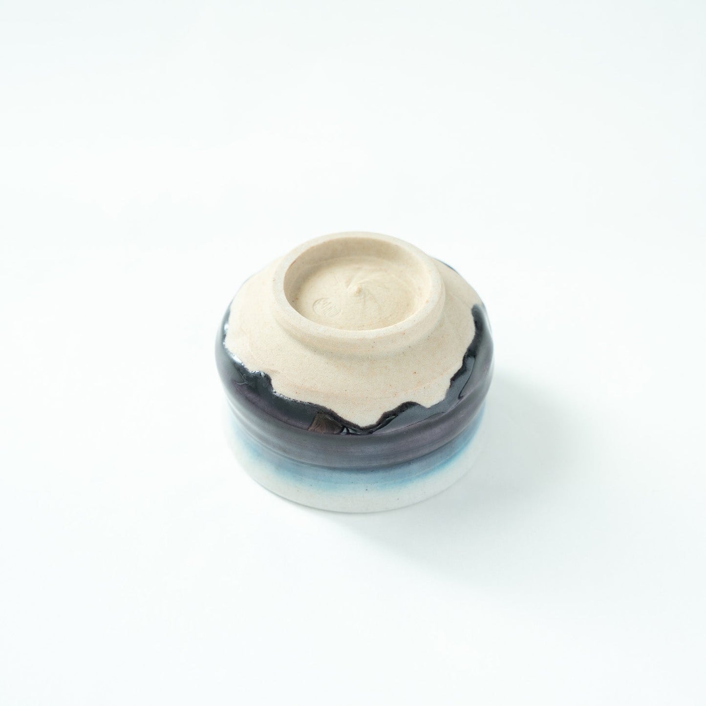 Inverted view of the GUINOMI, showcasing the precise craftsmanship of the unglazed foot against the dark glaze rim.