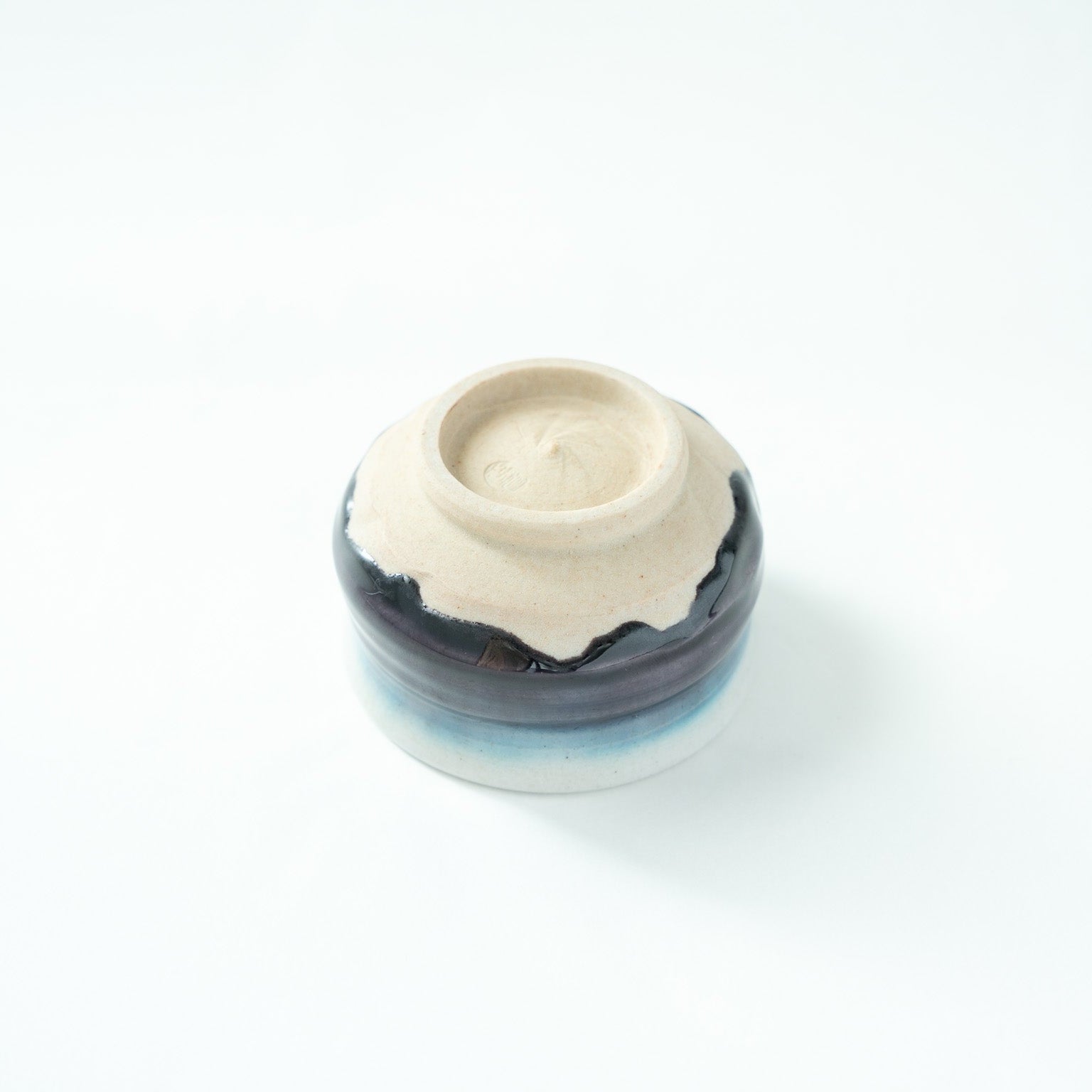Inverted view of the GUINOMI, showcasing the precise craftsmanship of the unglazed foot against the dark glaze rim.