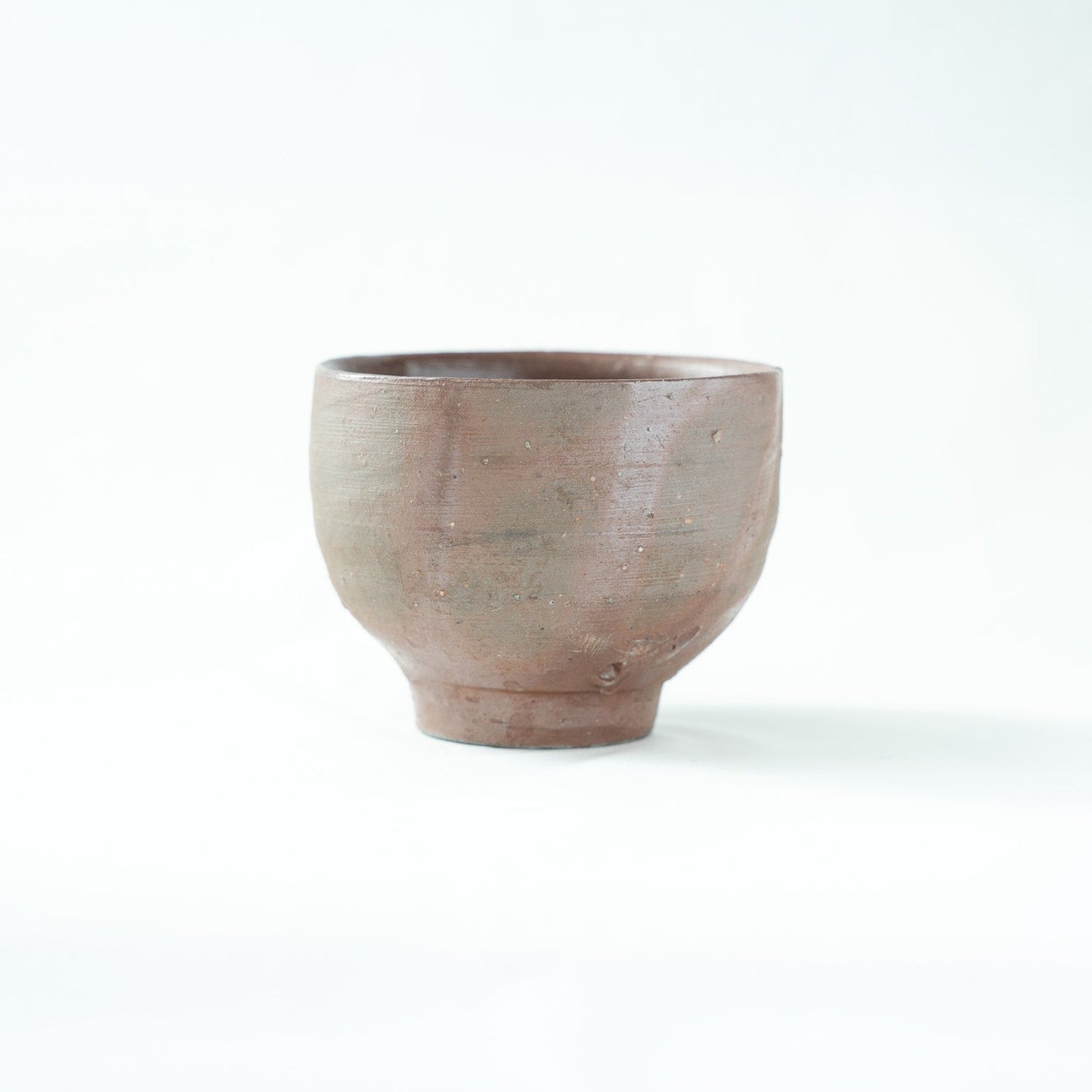 Alternate profile view of the unglazed ceramic cup, displaying the gentle horizontal wheel lines along its form.