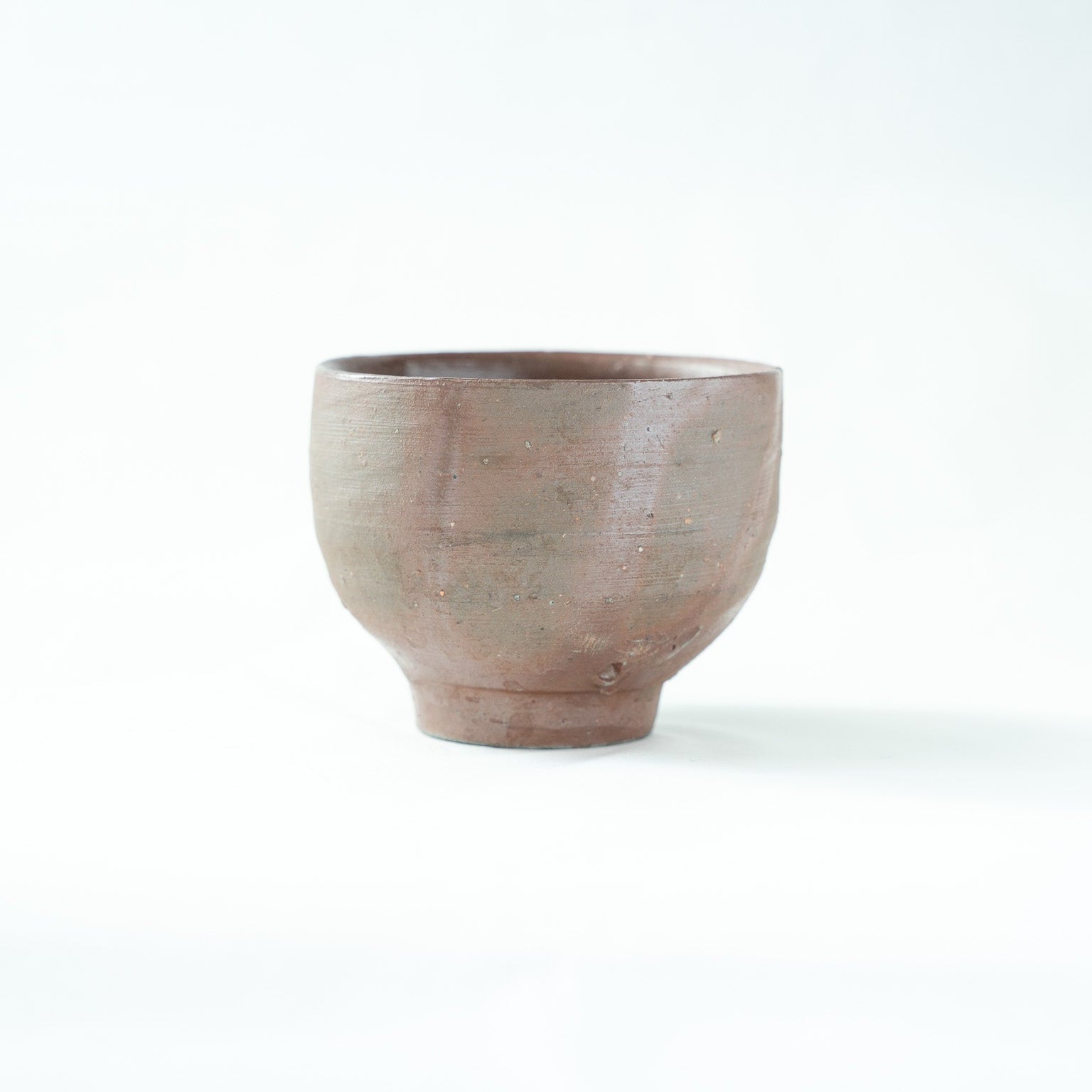 Alternate profile view of the unglazed ceramic cup, displaying the gentle horizontal wheel lines along its form.