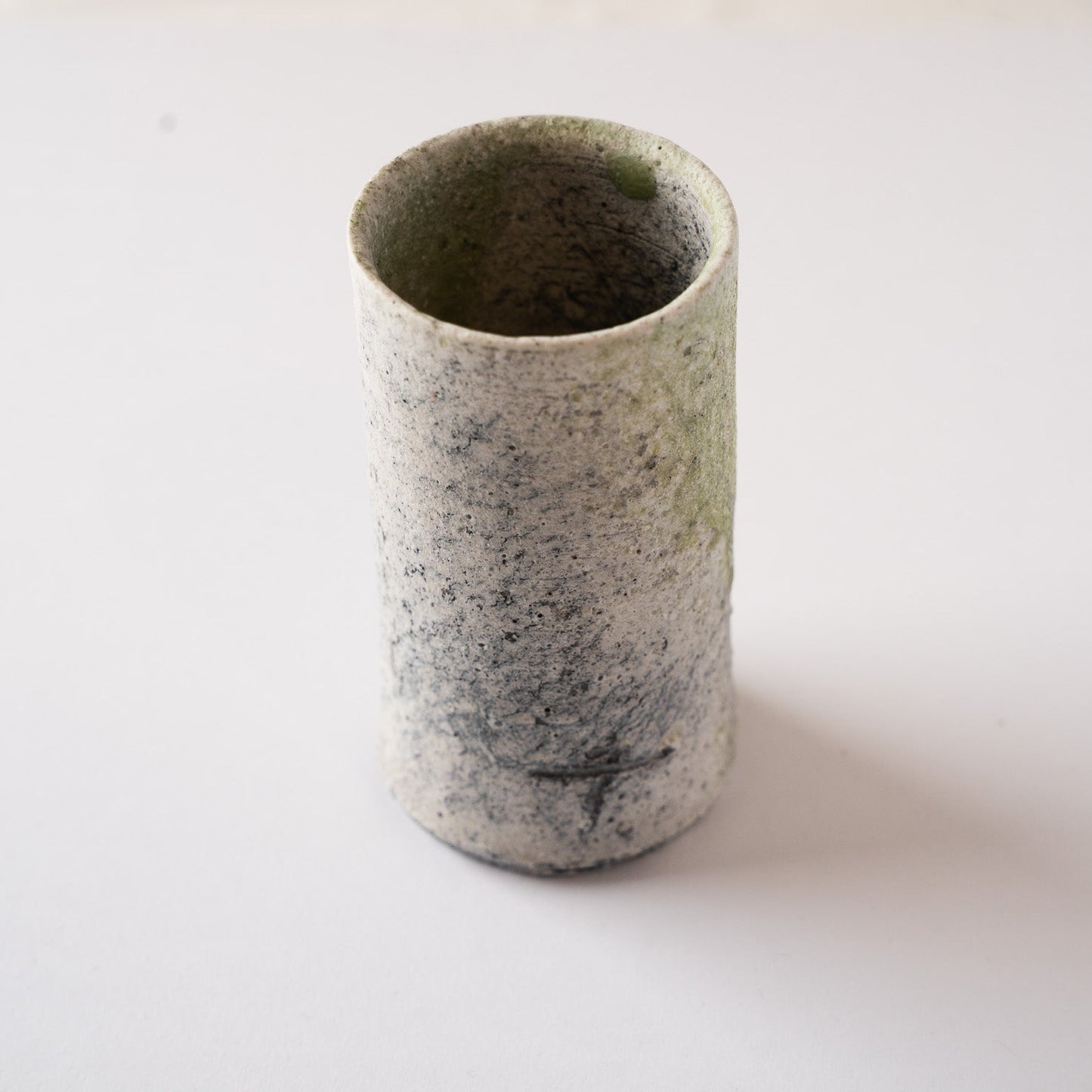 High-angle view focusing on the dark kiln effects and the incised artist's mark on the back of the cylindrical YUNOMI tea cup by Yui Tsujimura.