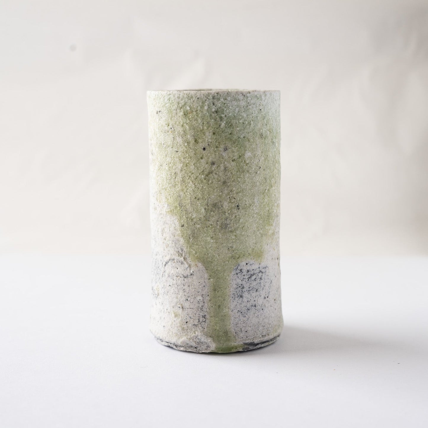 Straight-on view of the main facade of the cylindrical YUNOMI cup by Yui Tsujimura, accentuating the perfect vertical stream of green vidro glaze.