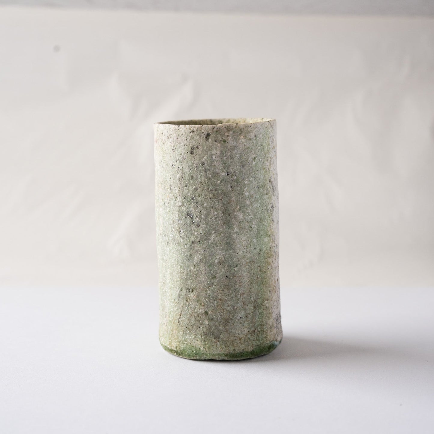 Front view of Yui Tsujimura's cylindrical natural ash glaze YUNOMI cup, showing an atmospheric green mist texture and a dark green vidro line at the lower edge.