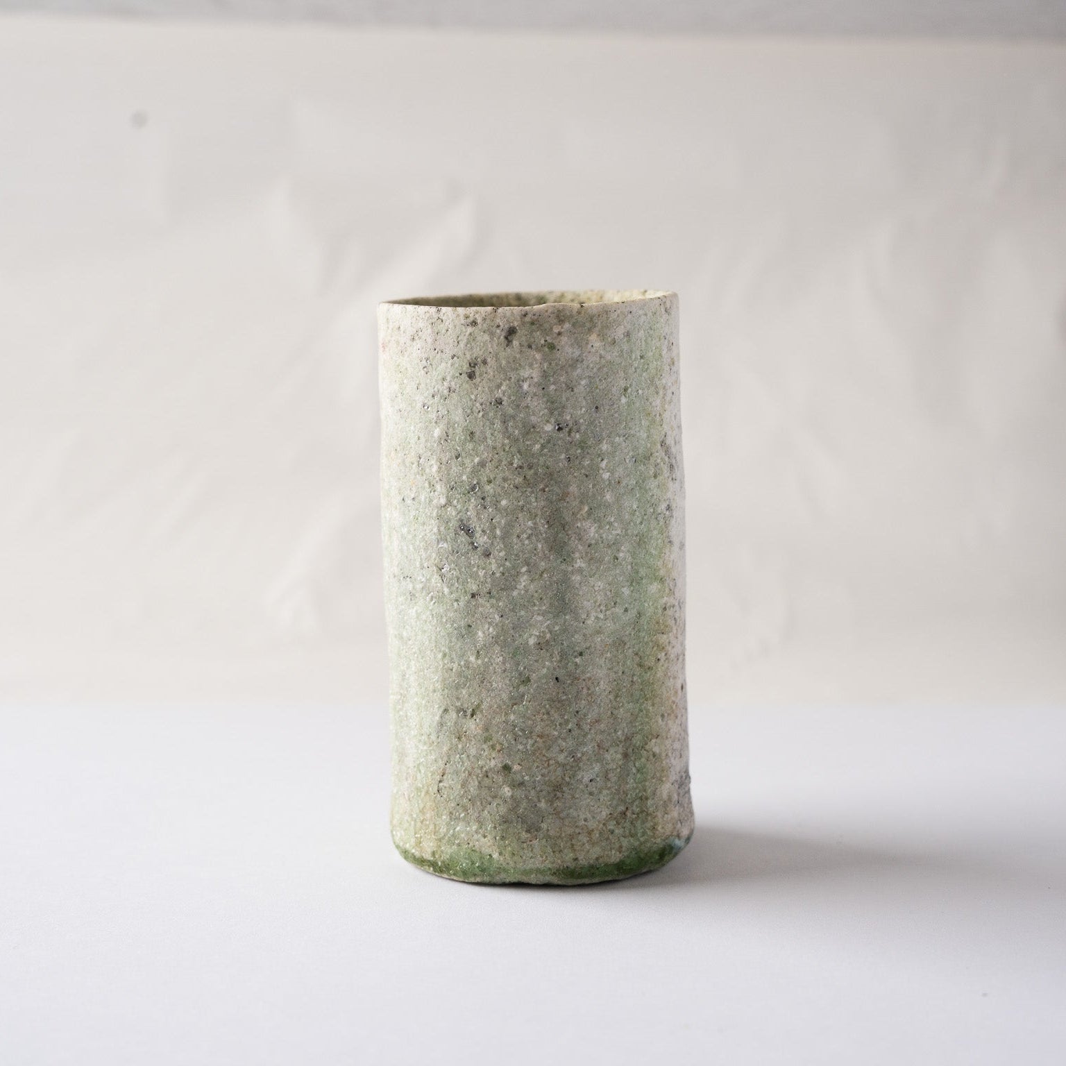 Front view of Yui Tsujimura's cylindrical natural ash glaze YUNOMI cup, showing an atmospheric green mist texture and a dark green vidro line at the lower edge.