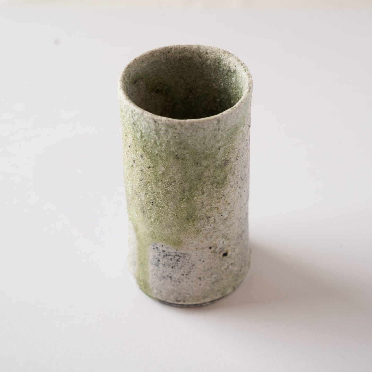 High-angle view of a tall, cylindrical natural ash glaze YUNOMI cup by Yui Tsujimura, showing a smooth stream of green vidro glaze running down the textured white surface.