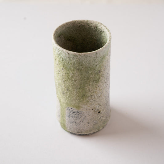 High-angle view of a tall, cylindrical natural ash glaze YUNOMI cup by Yui Tsujimura, showing a smooth stream of green vidro glaze running down the textured white surface.