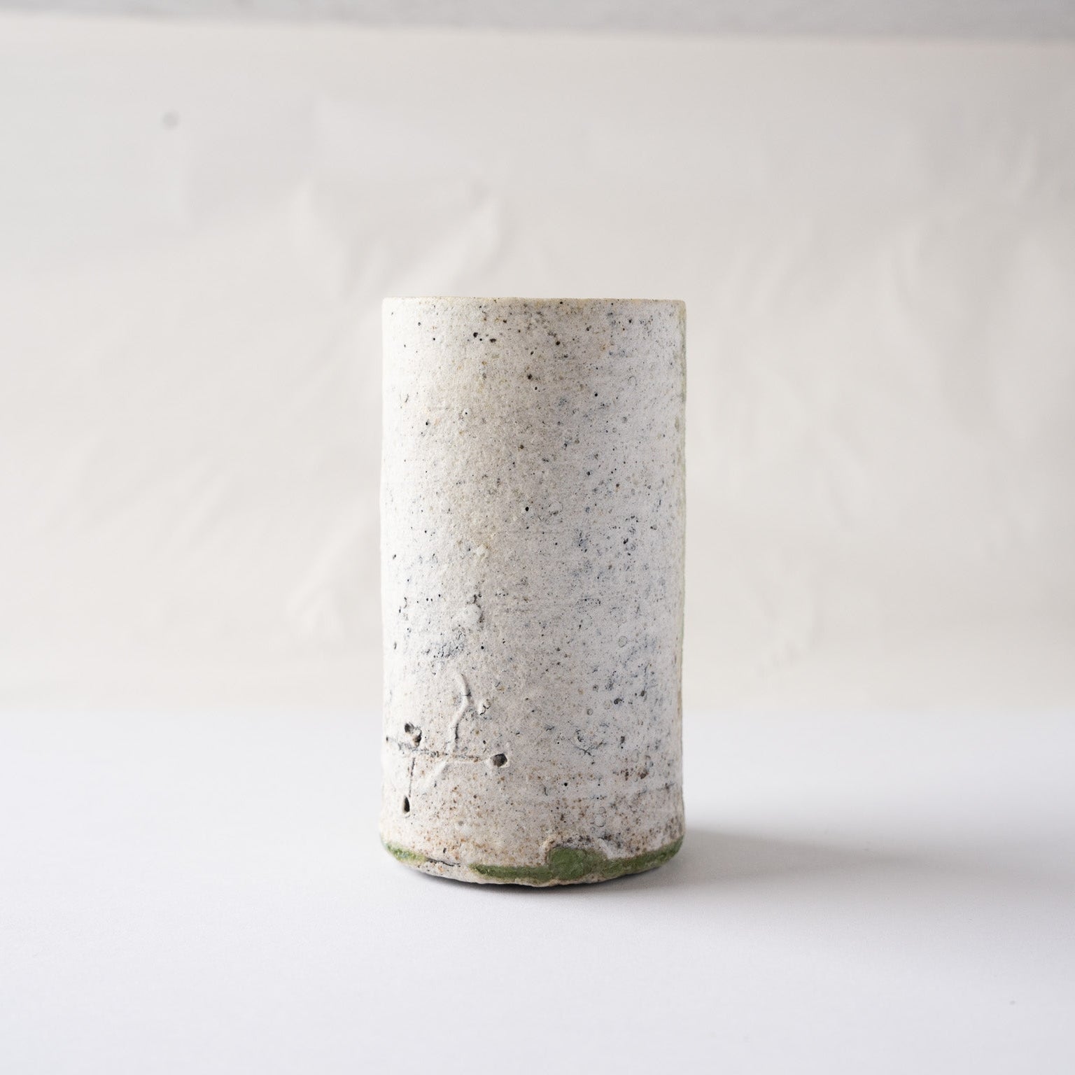 Back view of the cylindrical YUNOMI tea cup by Yui Tsujimura, displaying the rustic white granite texture and the artist’s incised mark near the bottom.