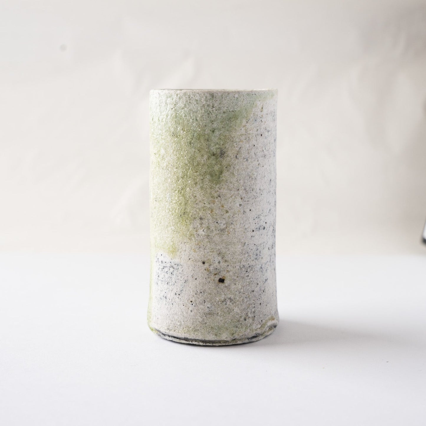 Side view of the natural ash glaze cylindrical YUNOMI by Yui Tsujimura, capturing the soft mist-like green coloration blending into the white stone texture.