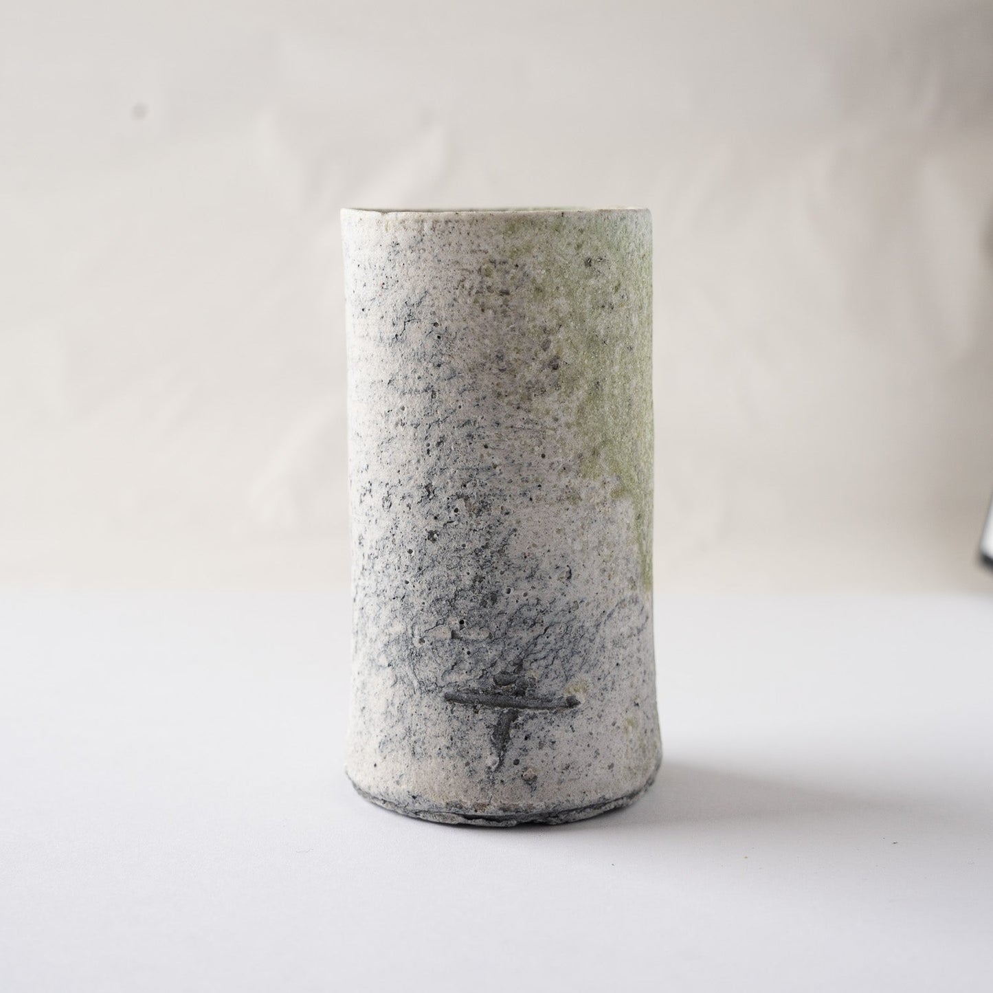 Studio portrait of the dark-toned side of Yui Tsujimura’s cylindrical YUNOMI, detailing the strong horizontal incised artist sign amid charcoal kiln scorches.