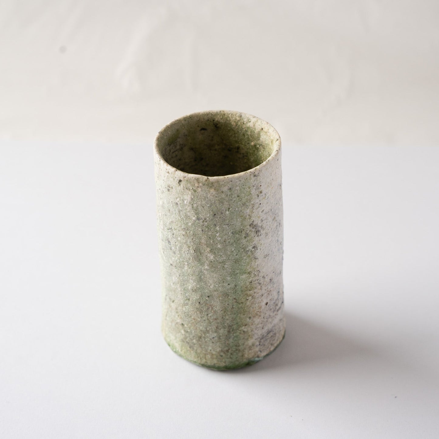 Three-quarter high-angle view of the green-glazed side of Yui Tsujimura’s cylindrical YUNOMI cup, illustrating the gentle surface movement.