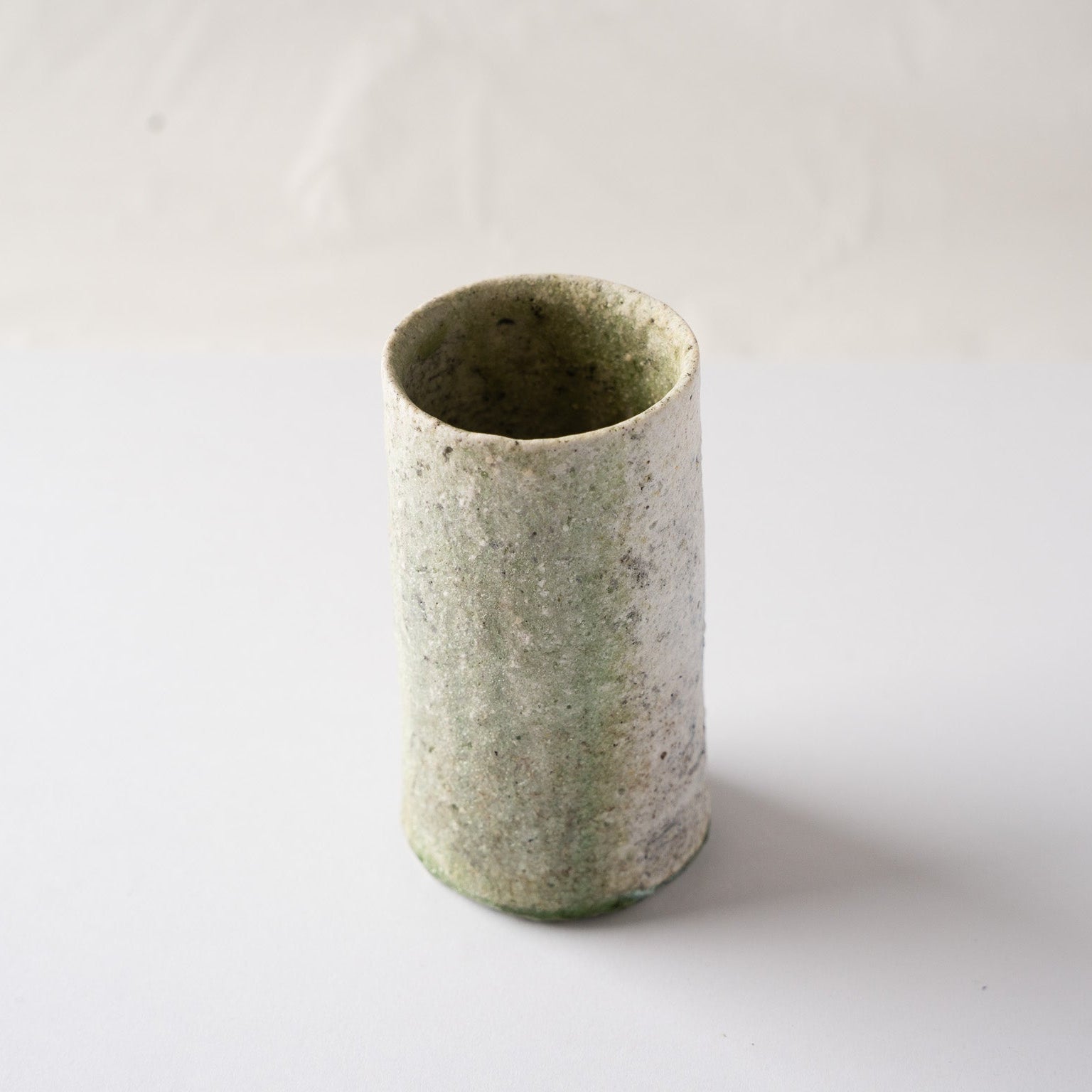 Three-quarter high-angle view of the green-glazed side of Yui Tsujimura’s cylindrical YUNOMI cup, illustrating the gentle surface movement.