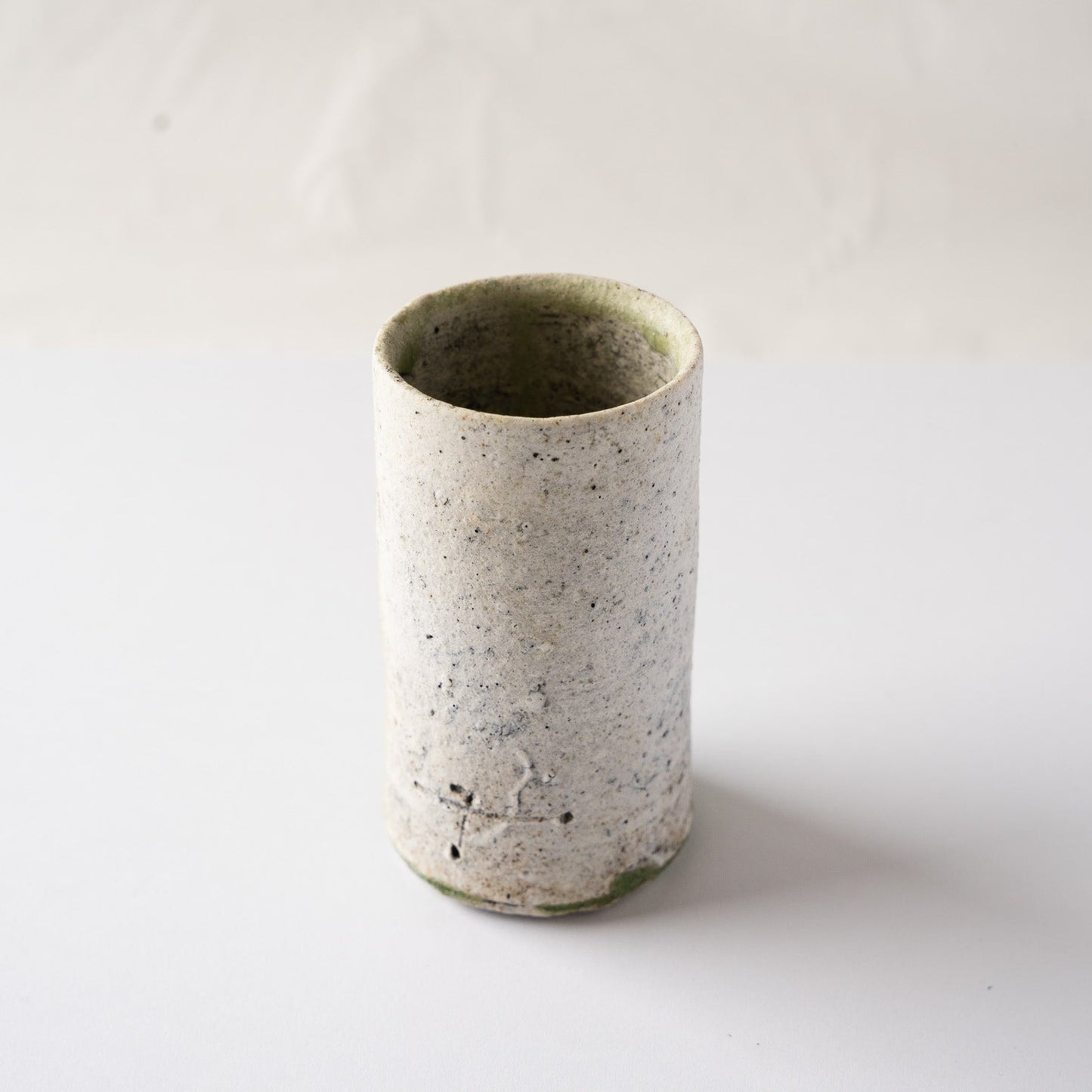 Three-quarter high-angle view of the white facade of the cylindrical YUNOMI cup by Yui Tsujimura, highlighting its column-like architectural silhouette.