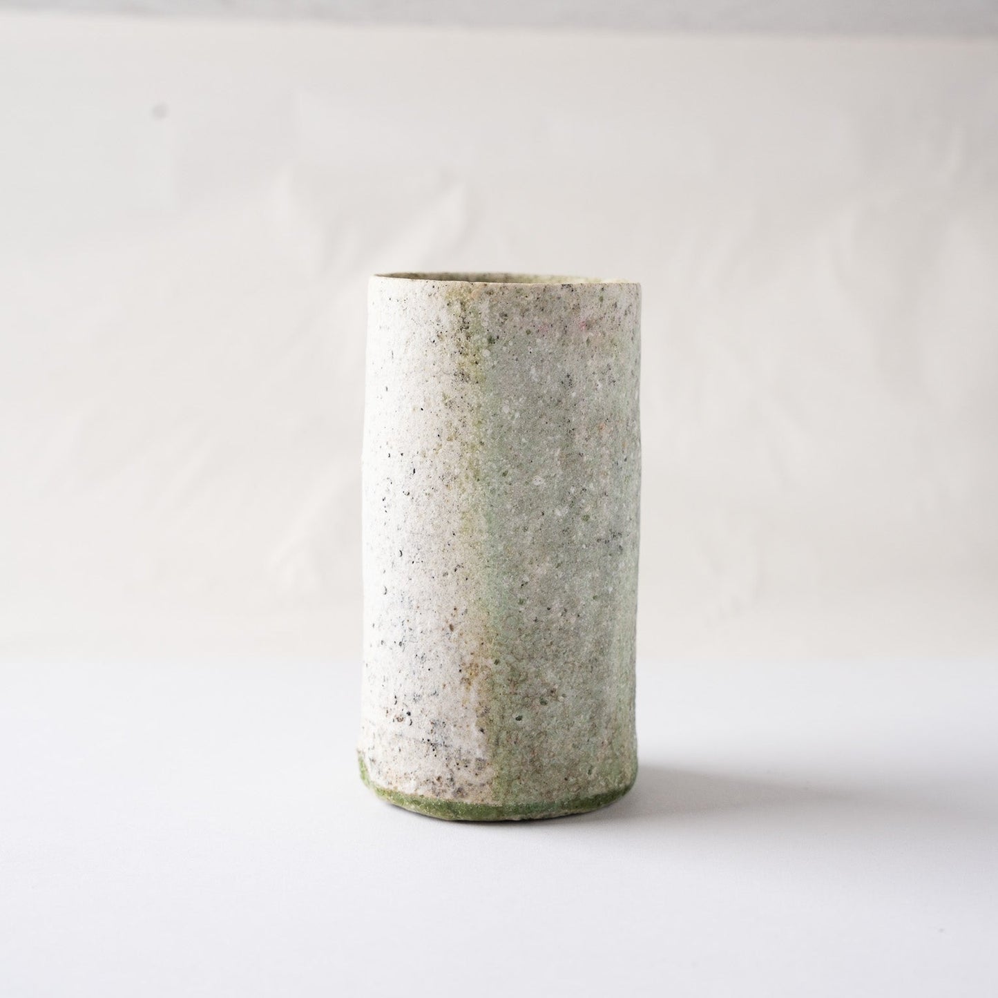 Profile view of Yui Tsujimura’s tall YUNOMI cup, capturing the subtle tonal boundary between the white clay face and the olive-green ash glaze layer.
