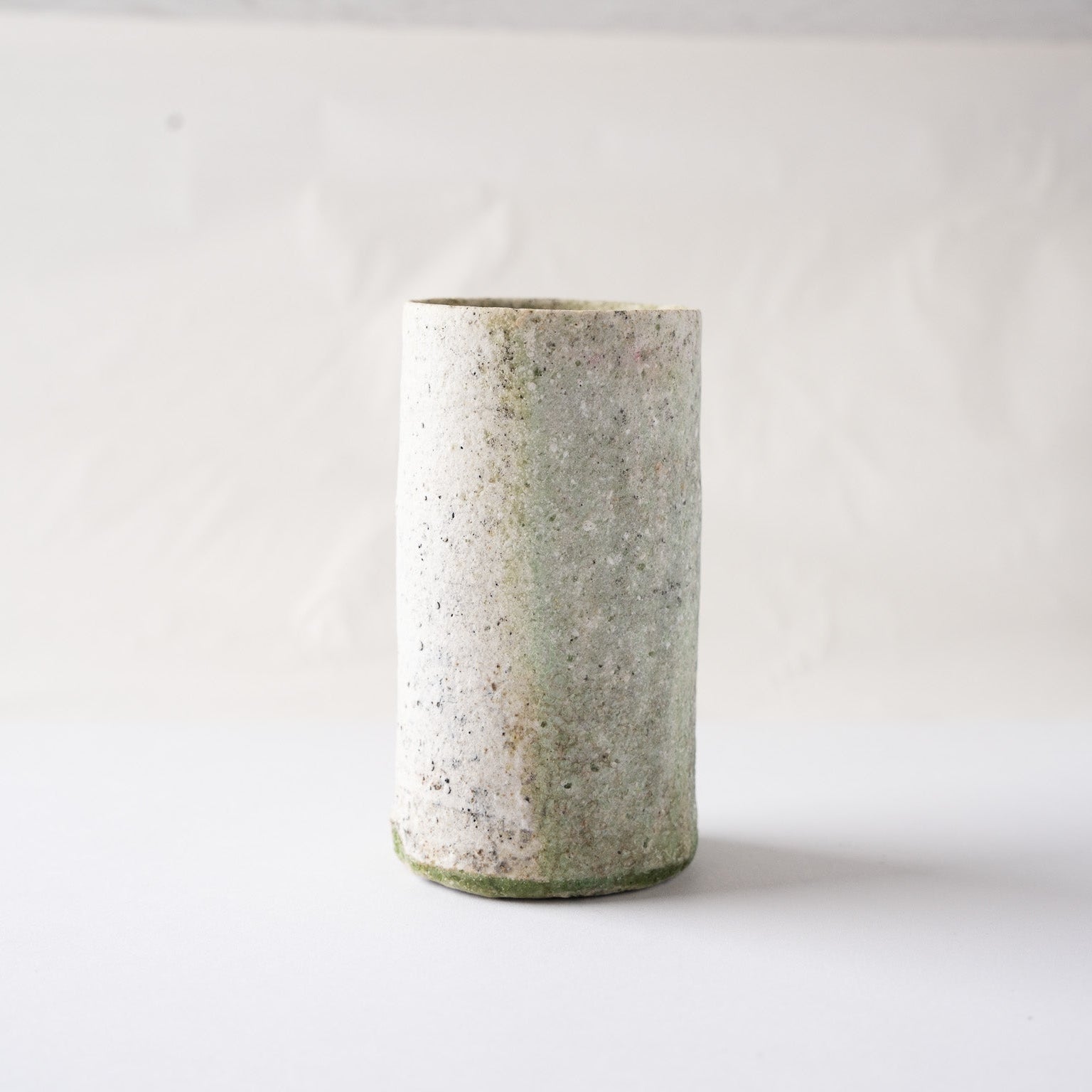 Profile view of Yui Tsujimura’s tall YUNOMI cup, capturing the subtle tonal boundary between the white clay face and the olive-green ash glaze layer.
