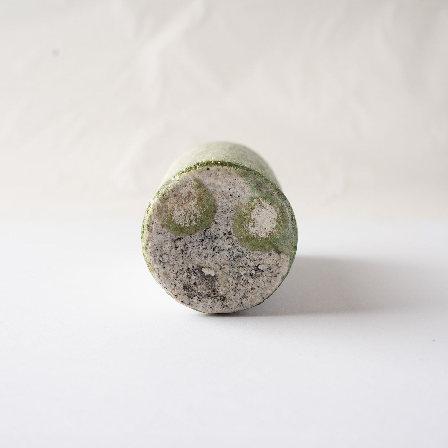 Close-up of the unglazed flat base of Yui Tsujimura's YUNOMI cup, showing a unique formation of two round, emerald-green vidro glaze crystals.