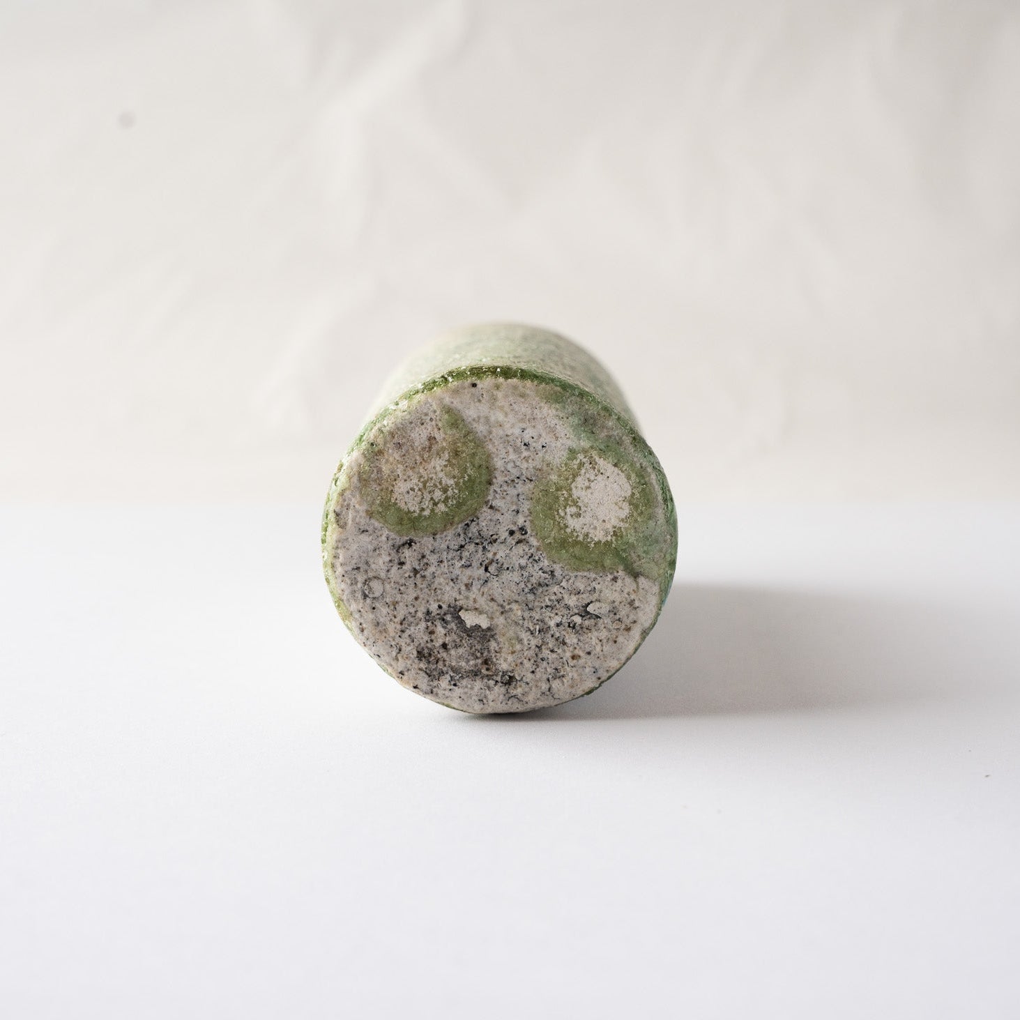 Close-up of the unglazed flat base of Yui Tsujimura's YUNOMI cup, showing a unique formation of two round, emerald-green vidro glaze crystals.