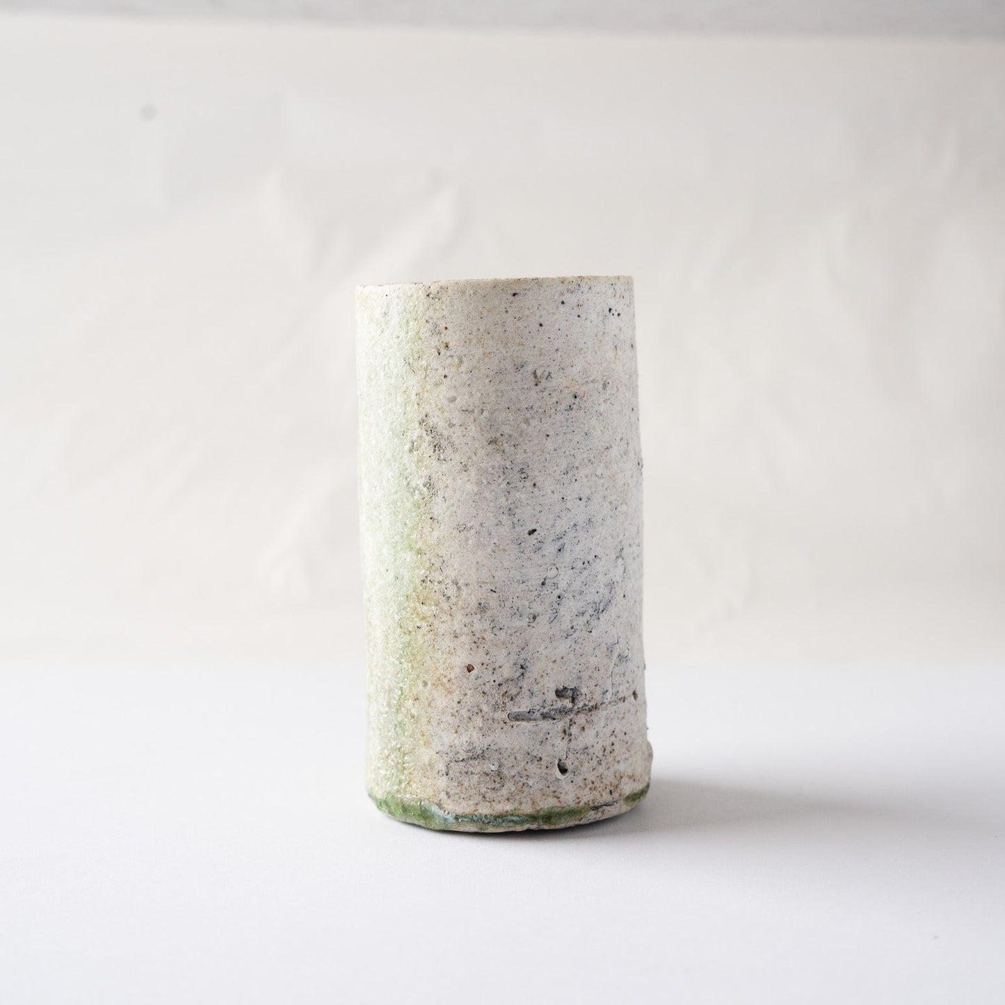 Side view of the cylindrical natural ash glaze YUNOMI cup by Yui Tsujimura, featuring the mineral-rich white clay surface with a faint green undertone.