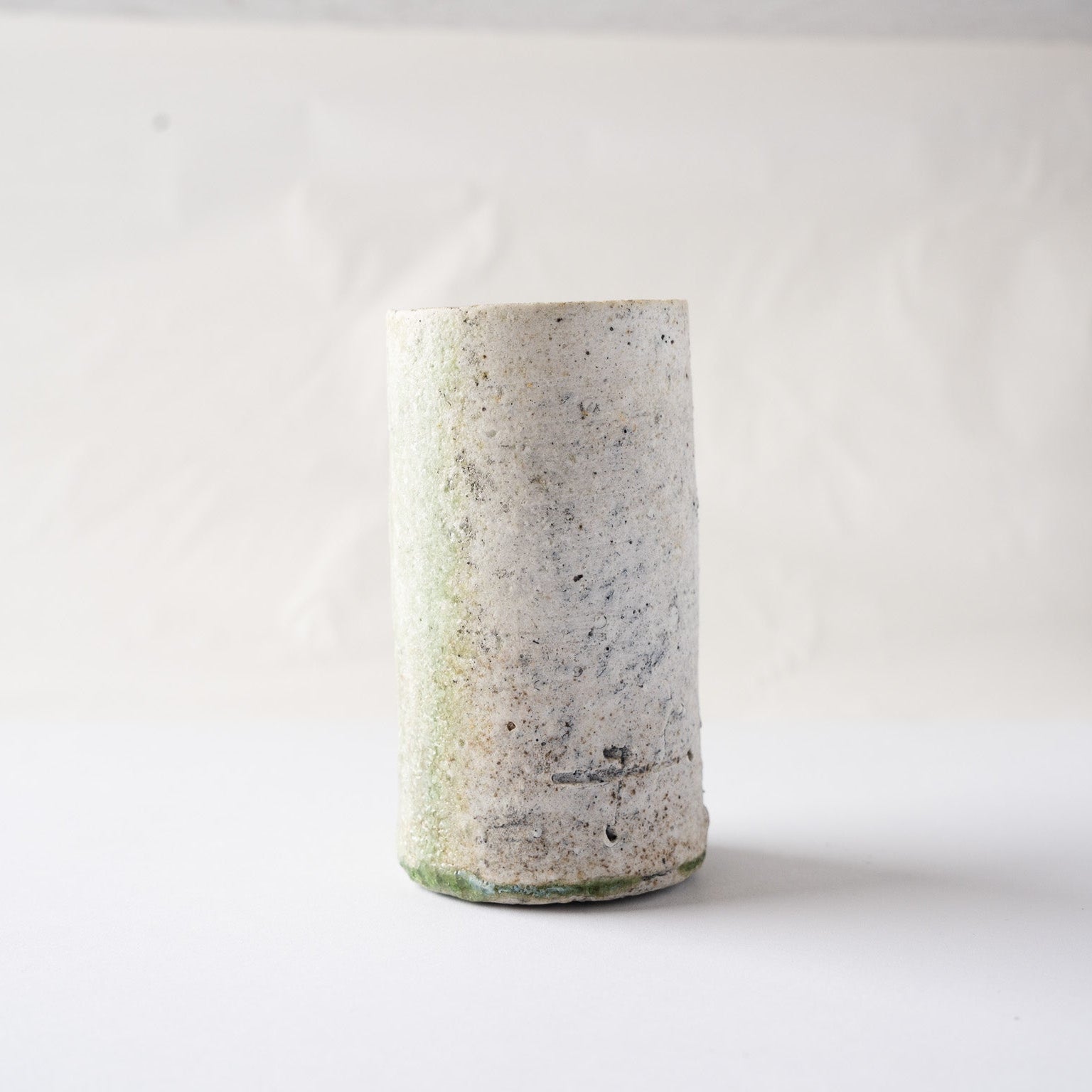 Side view of the cylindrical natural ash glaze YUNOMI cup by Yui Tsujimura, featuring the mineral-rich white clay surface with a faint green undertone.