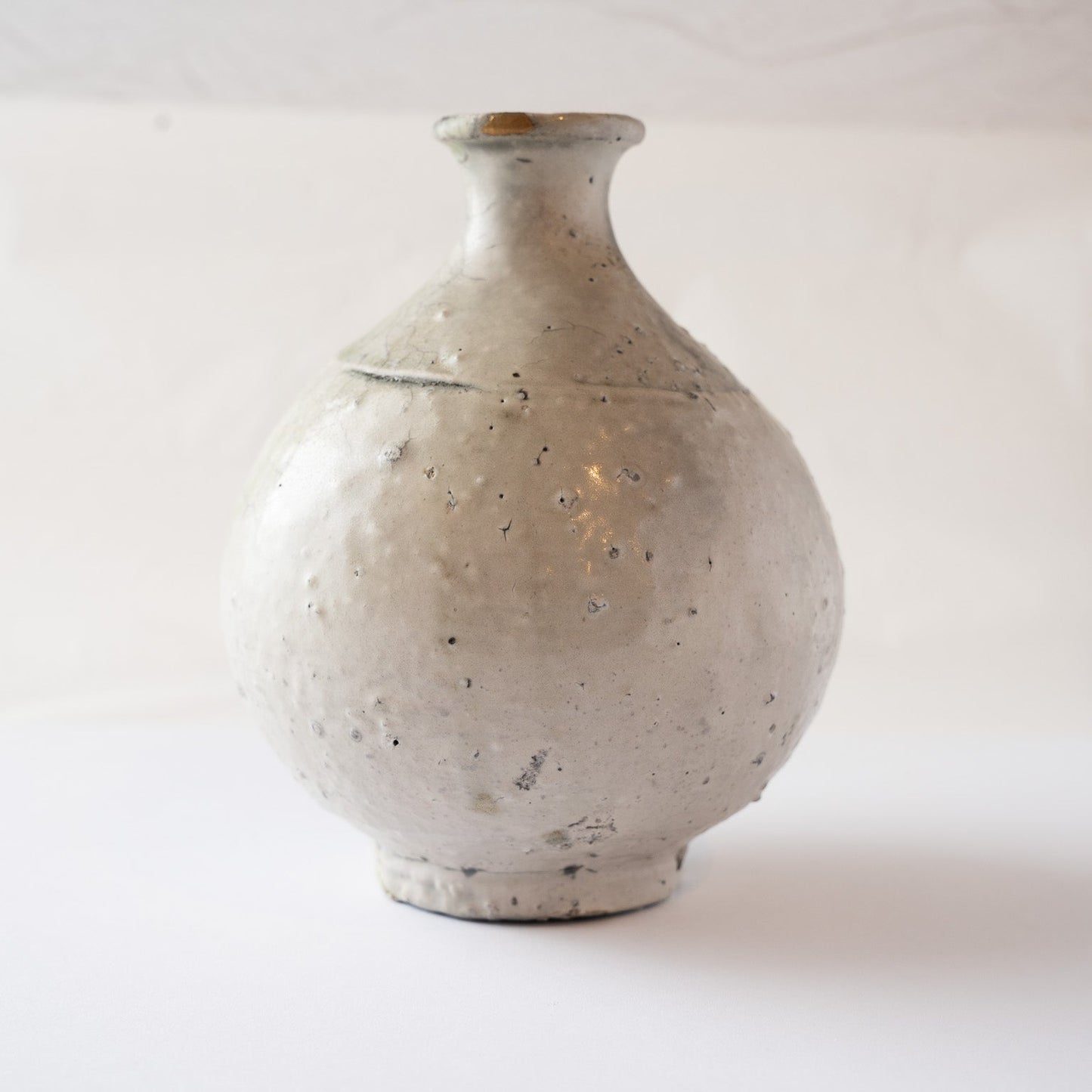 Front view of Yui Tsujimura’s spherical natural ash glaze TOKKURI sake flask, featuring a chalky white clay body and a gold kintsugi repair on the lip.