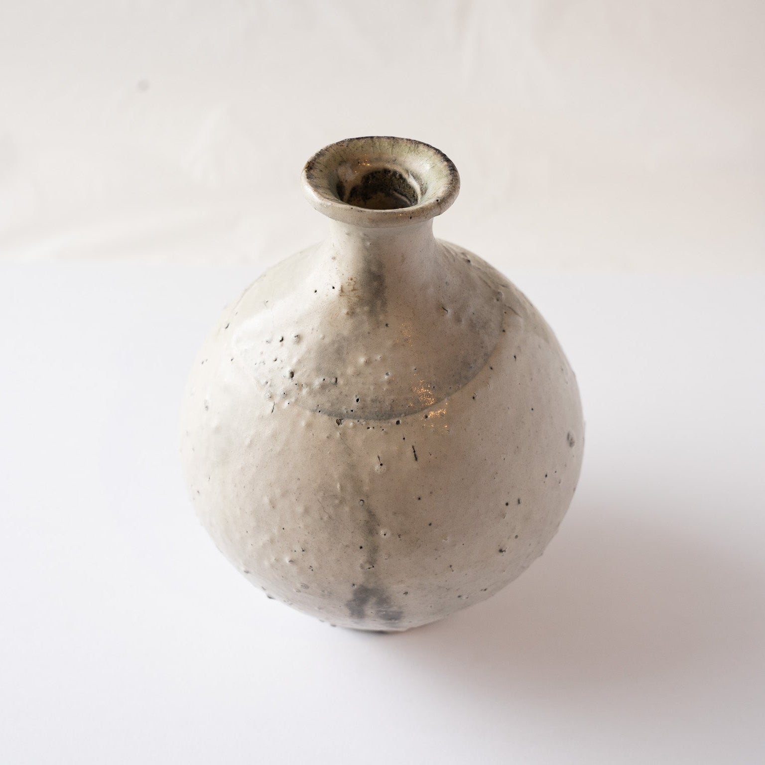 High-angle turned view of the spherical TOKKURI sake flask by Yui Tsujimura, highlighting soft charcoal smoke clouds on the ceramic body.