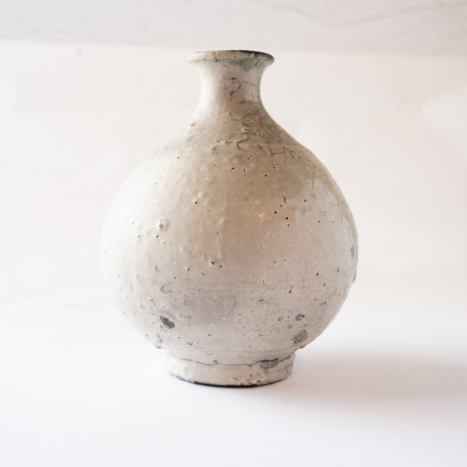 Rear view of the spherical ceramic TOKKURI flask by Yui Tsujimura, showing the soft textured white clay body with fine iron speckles.