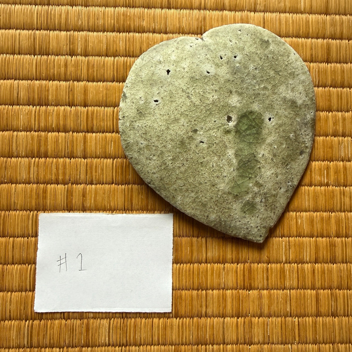 Underside of plate 1 from the natural ash glaze viburnum leaf dish set by Yui Tsujimura, showing raw earthy clay texture and a central vertical green glaze trace.