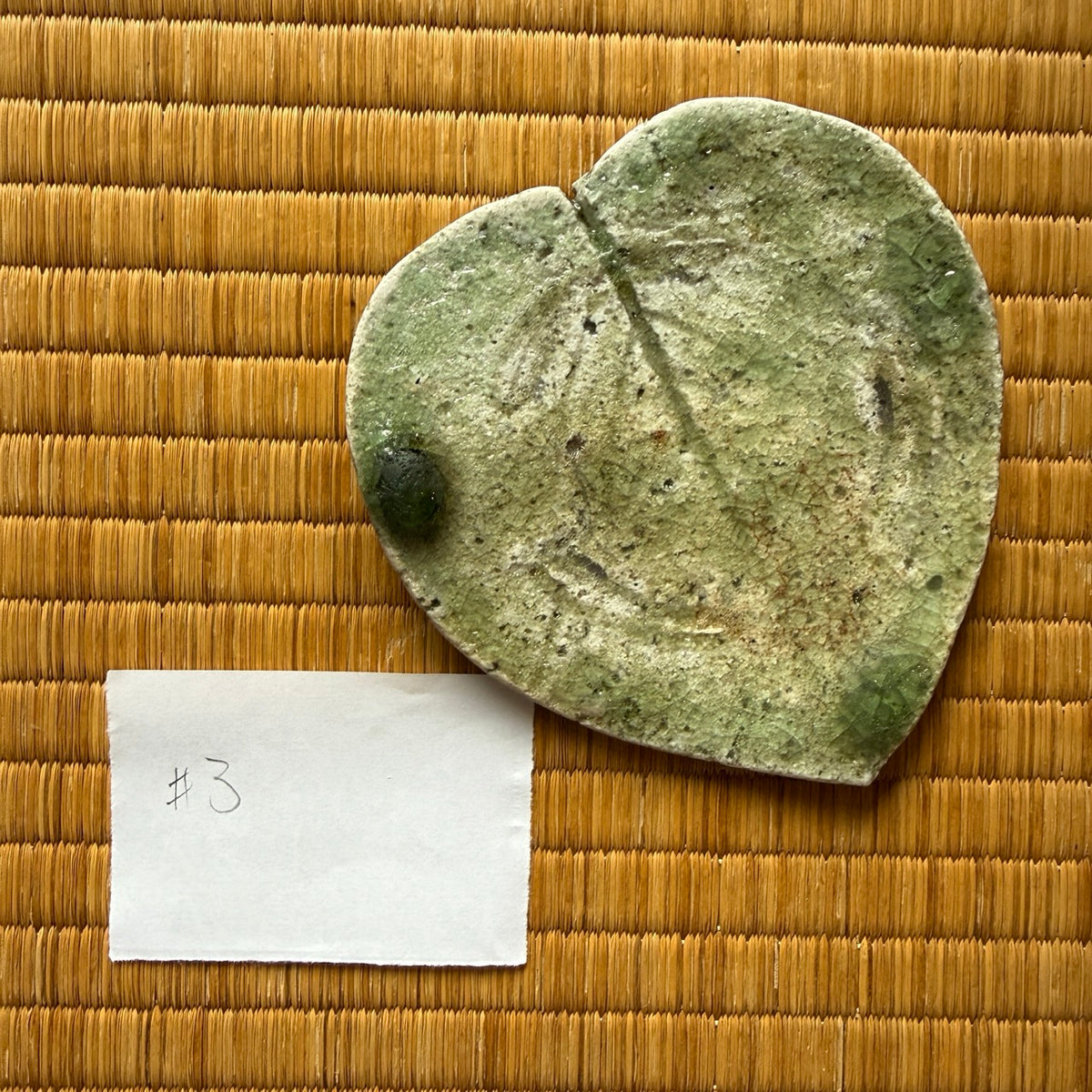 Top view of plate 3 from Yui Tsujimura’s natural ash glaze viburnum leaf dish set, featuring organic leaf vein engraving and a jewel-like dark green glass drop along the rim.