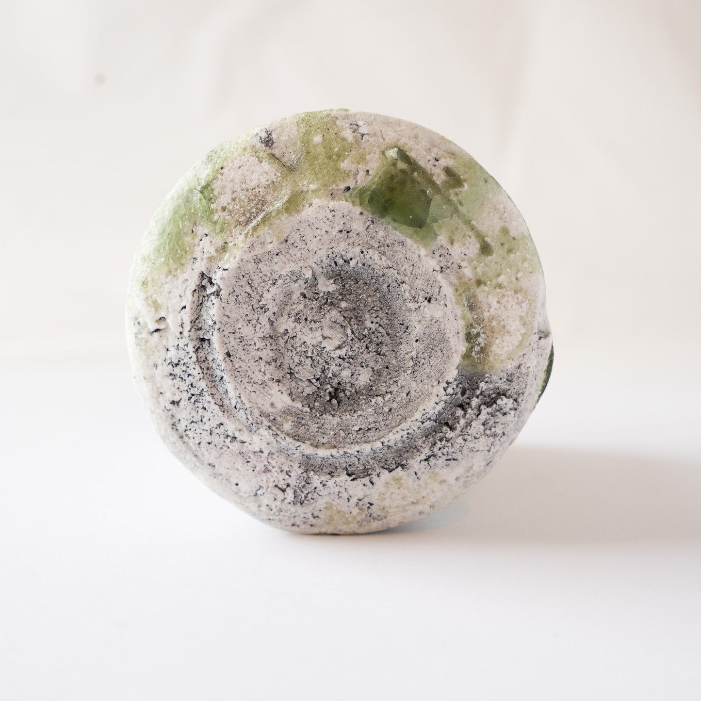 The unglazed base of a natural ash glaze YUNOMI cup by Yui Tsujimura, highlighting a striking jewel-like emerald green glass bead crystalized near the foot.