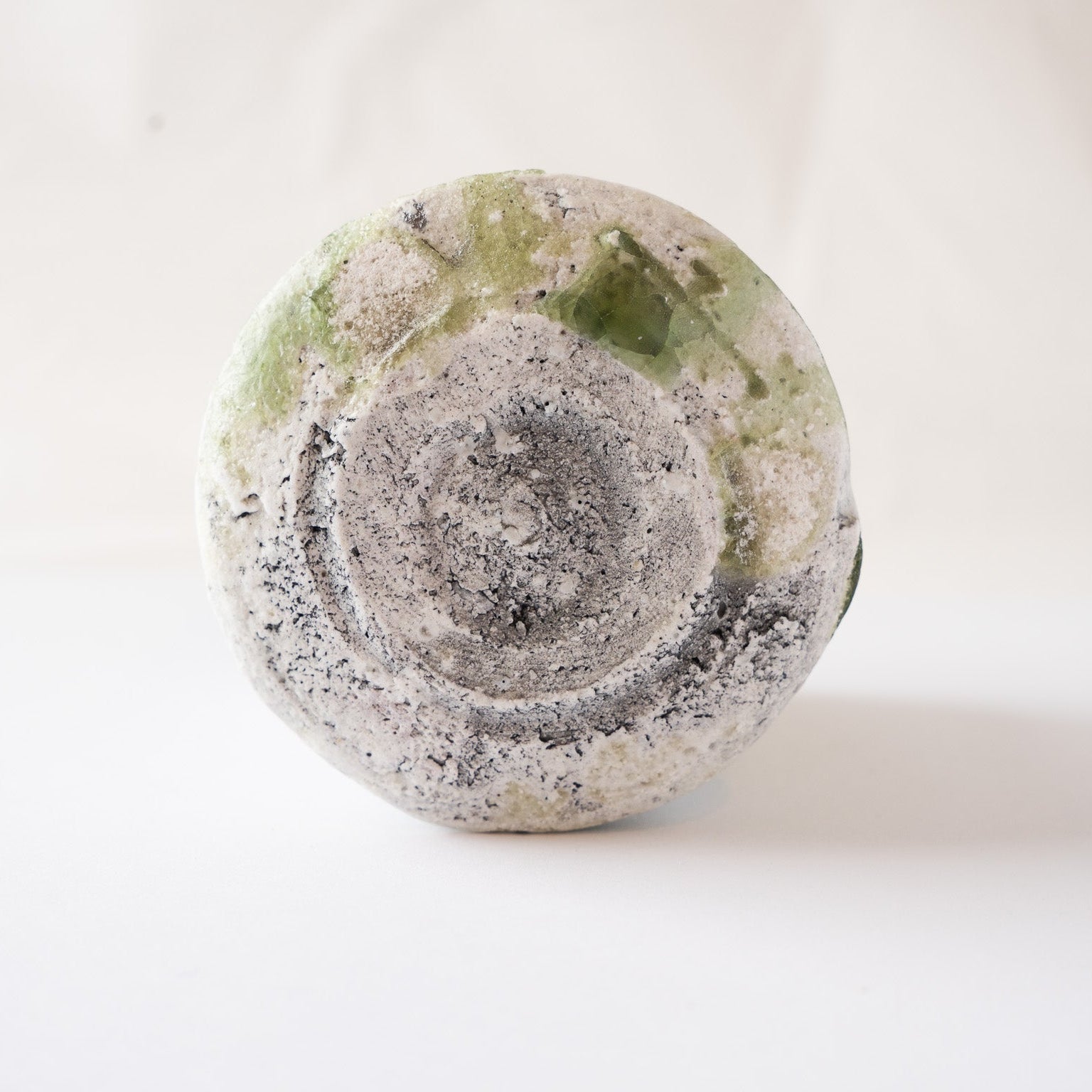 The unglazed base of a natural ash glaze YUNOMI cup by Yui Tsujimura, highlighting a striking jewel-like emerald green glass bead crystalized near the foot.