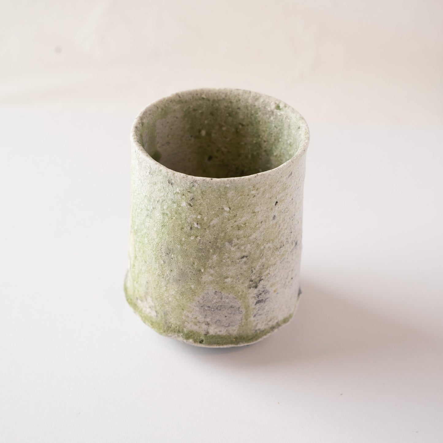 A slightly turned view of Yui Tsujimura’s natural ash glaze YUNOMI cup, highlighting the organic flow and dripping patterns of the pale green vidro glaze.