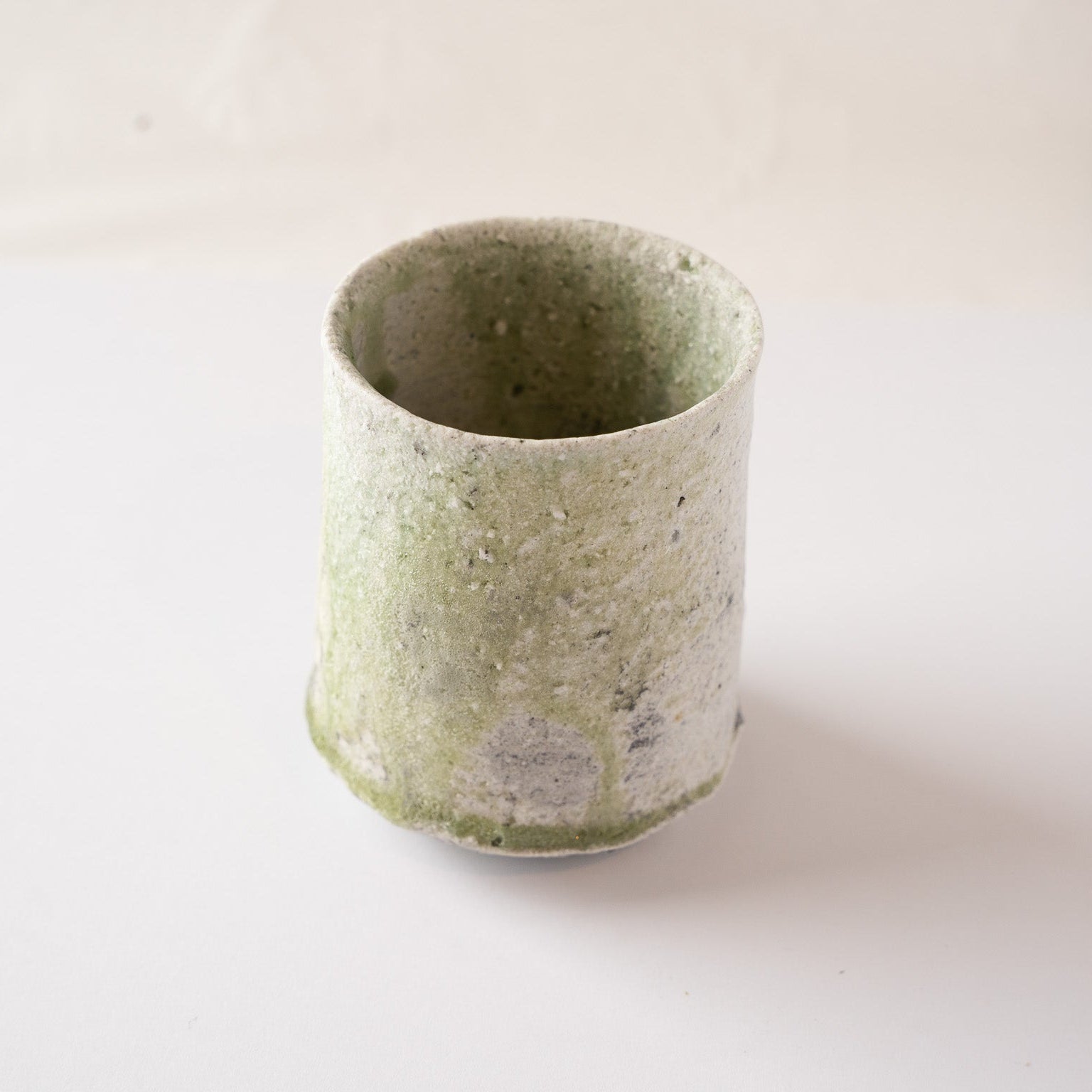 A slightly turned view of Yui Tsujimura’s natural ash glaze YUNOMI cup, highlighting the organic flow and dripping patterns of the pale green vidro glaze.