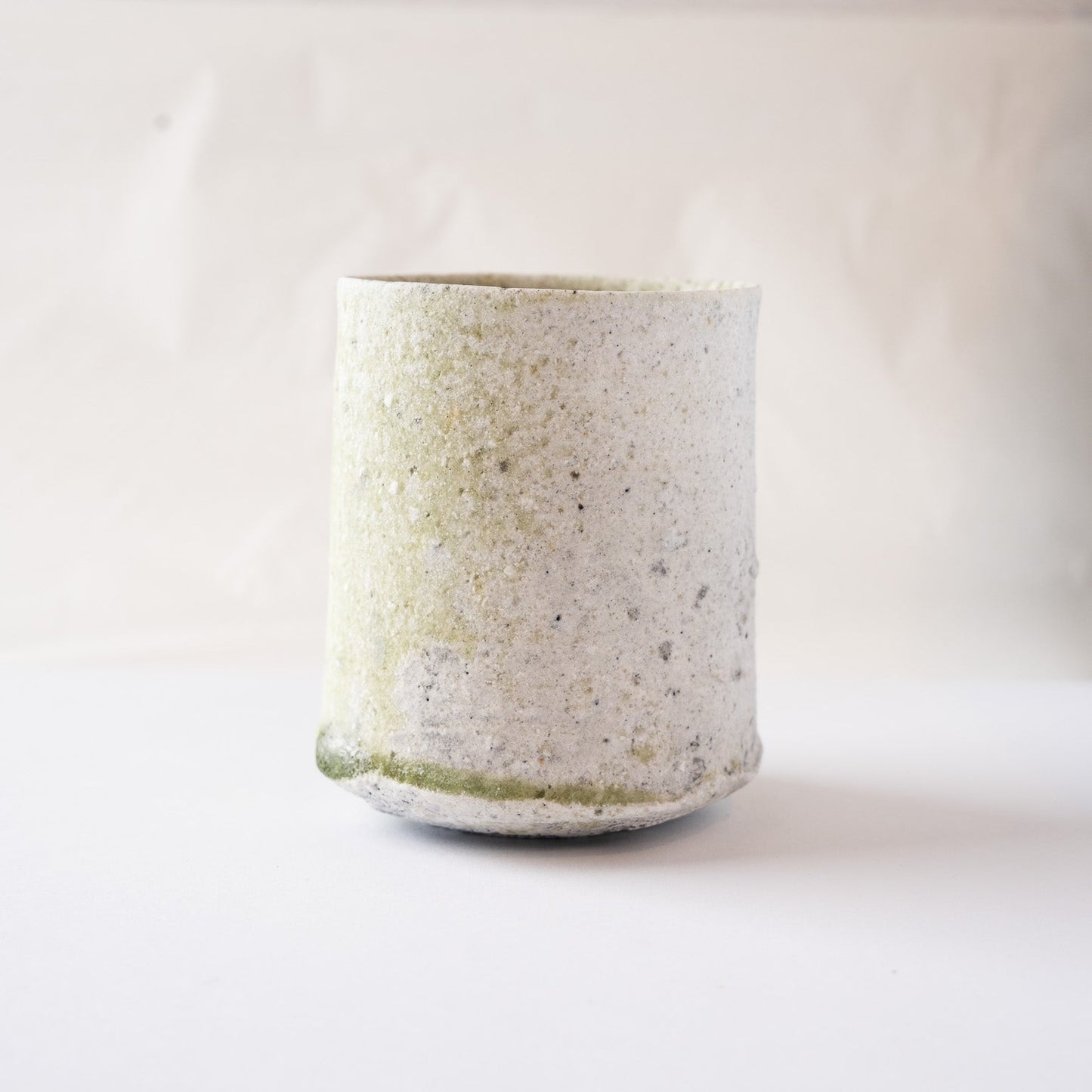 Front view of Yui Tsujimura’s natural ash glaze YUNOMI cup, focusing on the side where the pale green natural ash glaze spreads softly across the ceramic surface.