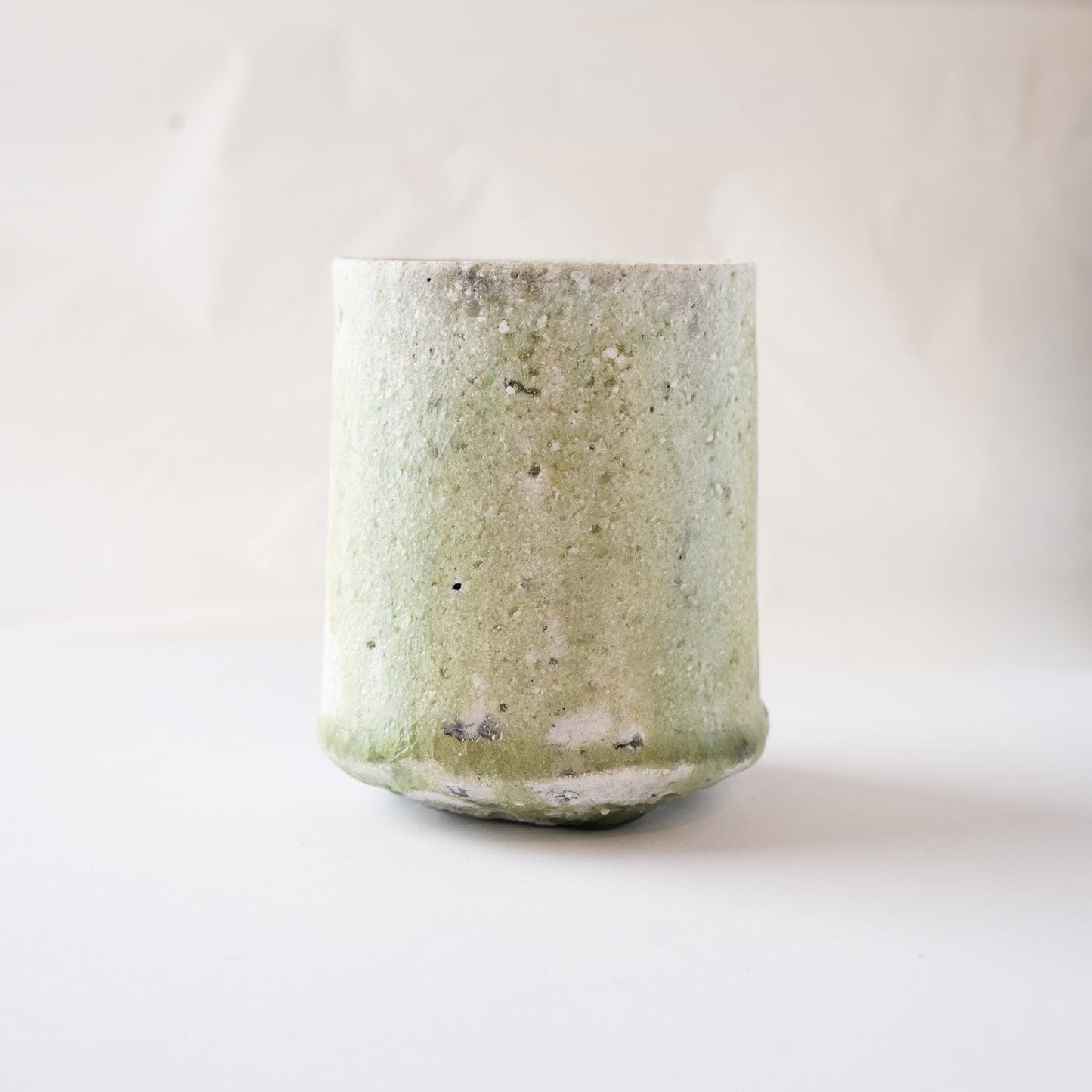 Front view of Yui Tsujimura’s natural ash glaze YUNOMI cup, focusing on the side where the pale green natural ash glaze spreads softly across the ceramic surface.