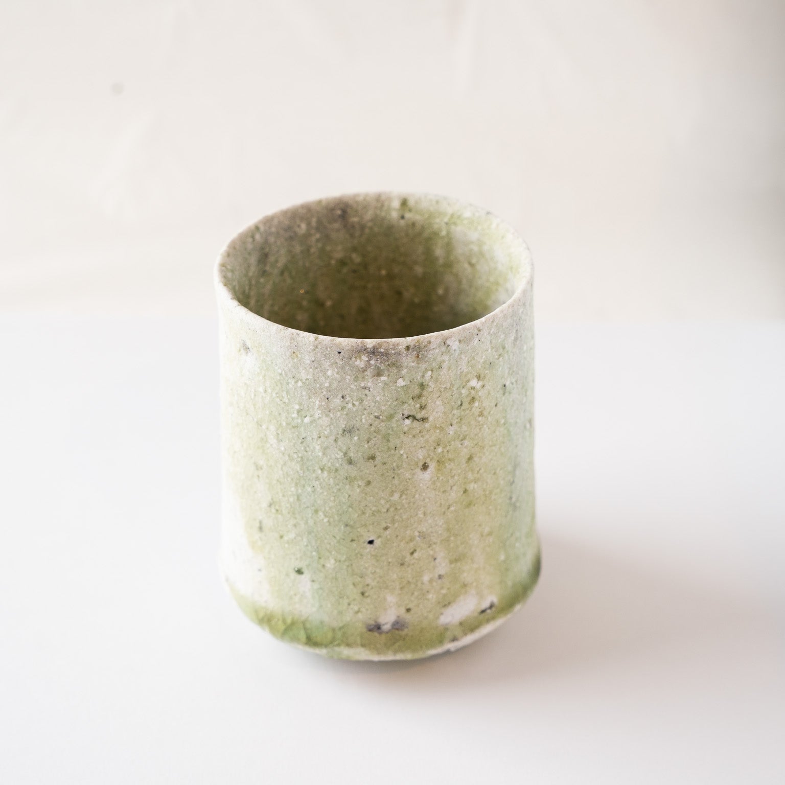 High-angle perspective of the green-glazed side of Yui Tsujimura’s YUNOMI cup, showing the fine mineral speckles and tactile surface quality.